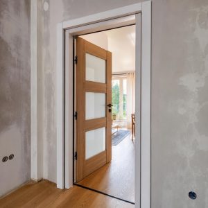 Biała futryna nakładkowa zamontowana na starej ościeżnicy w mieszkaniu, z otwartym skrzydłem pokazującym światło przejścia.