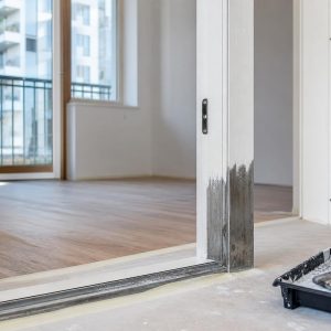 Metalowa futryna drzwi wewnętrznych w mieszkaniu podczas renowacji, z oczyszczonym dolnym narożnikiem i świeżo pomalowaną powierzchnią.